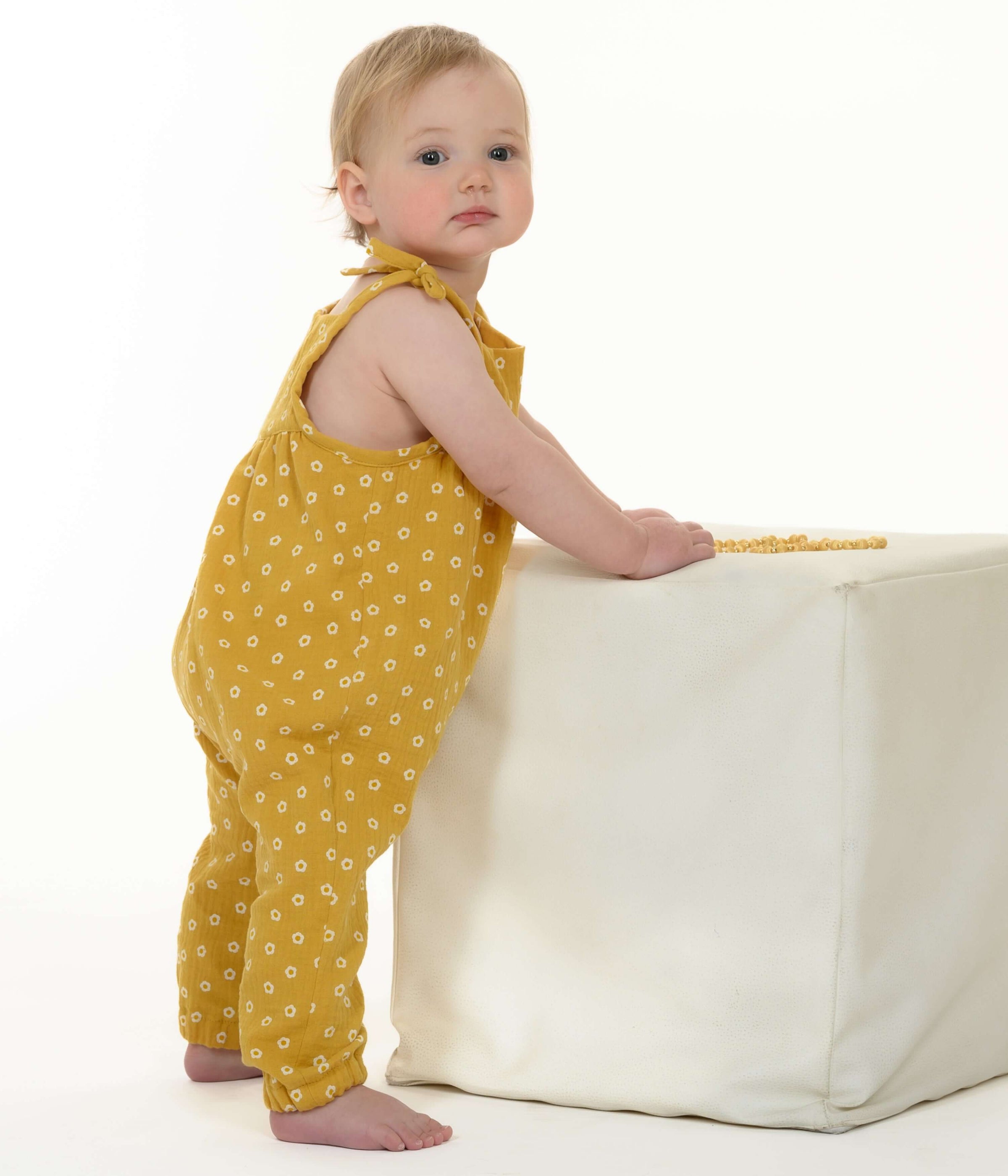 Schnittmuster Baby Overall Jumpsuit NELE – Kleinkind in gelbem Overall mit Pünktchen, stehend an einem weißen Würfel.