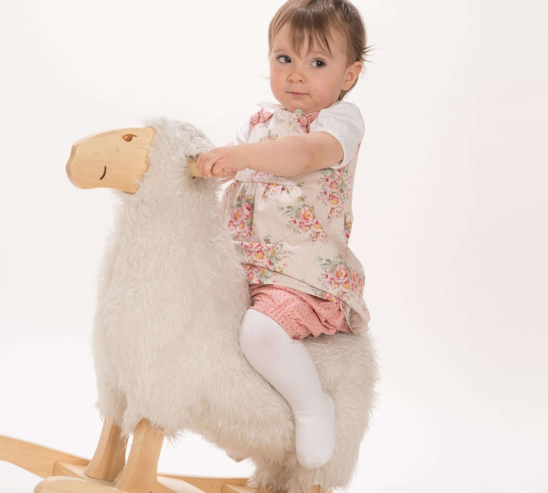 Schnittmuster Baby Twinset Babykleid Hängerchen und Pumphose CLARA EMI - Baby auf einem Schaukelpferd in frühlingshaftem Outfit.