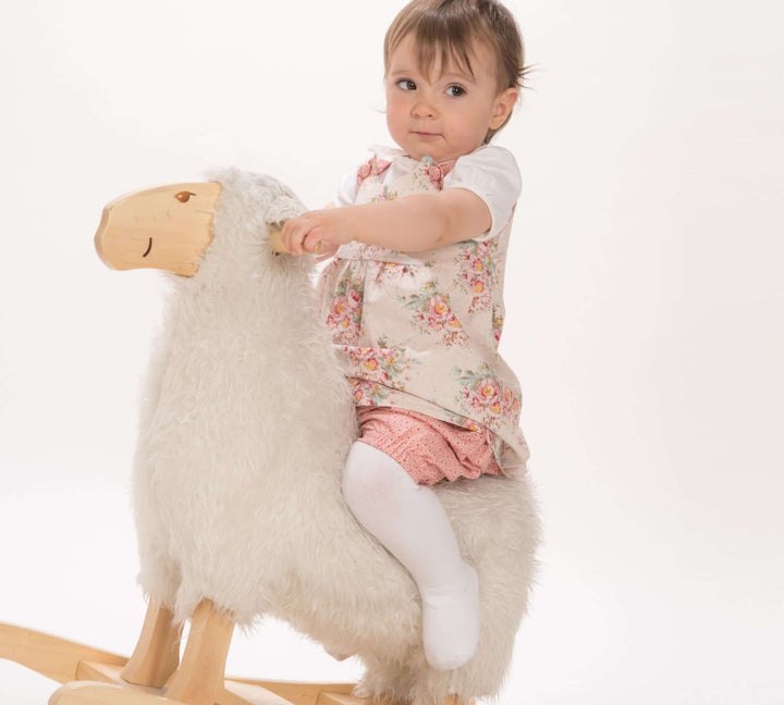 Schnittmuster Baby Twinset Babykleid Hängerchen und Pumphose CLARA EMI - Baby auf einem Schaukelpferd in frühlingshaftem Outfit.