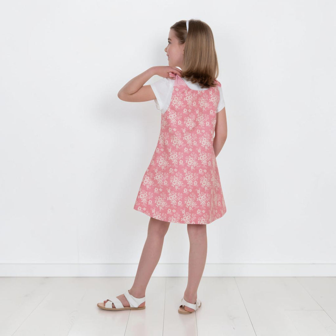 Mädchen kleidet sich im Trägerkleid PDF Schnittmuster ANTONIA – 3-in-1 Mädchenkleid 74/80–146/152, rosa mit Blütenmuster.