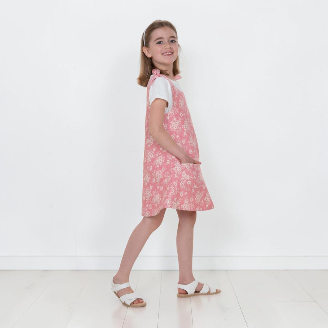 Mädchen trägt Trägerkleid PDF Schnittmuster ANTONIA in Blumenmuster, seitlicher Blick auf das 3-in-1 Kleid für 74/80–146/152.
