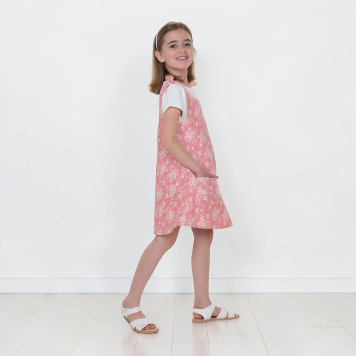 Mädchen trägt Trägerkleid PDF Schnittmuster ANTONIA in Blumenmuster, seitlicher Blick auf das 3-in-1 Kleid für 74/80–146/152.