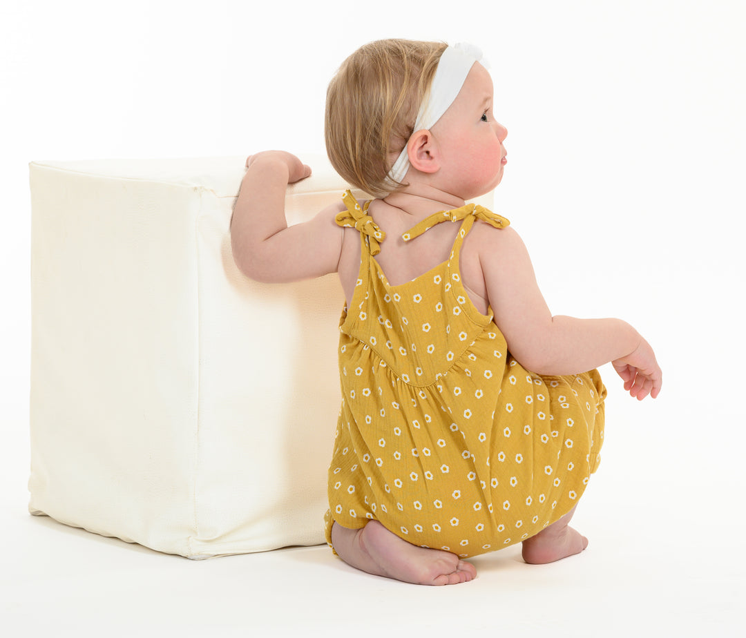 Schnittmuster Baby Overall – Kleinkind im gelben Overall mit Blumenmuster, sitzt auf einem weißen Würfel.