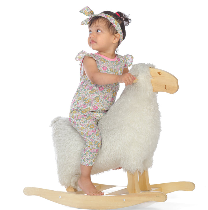 Mädchen im Schnittmuster Mädchenkleid MIA Jumpsuit, auf einem Schaukelpferd sitzend, mit Haarband.