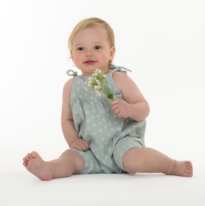 Schnittmuster Baby Mädchen Jumpsuit NELE – Kleinkind im blauen Overall mit Blumen, sitzend und lächelnd.