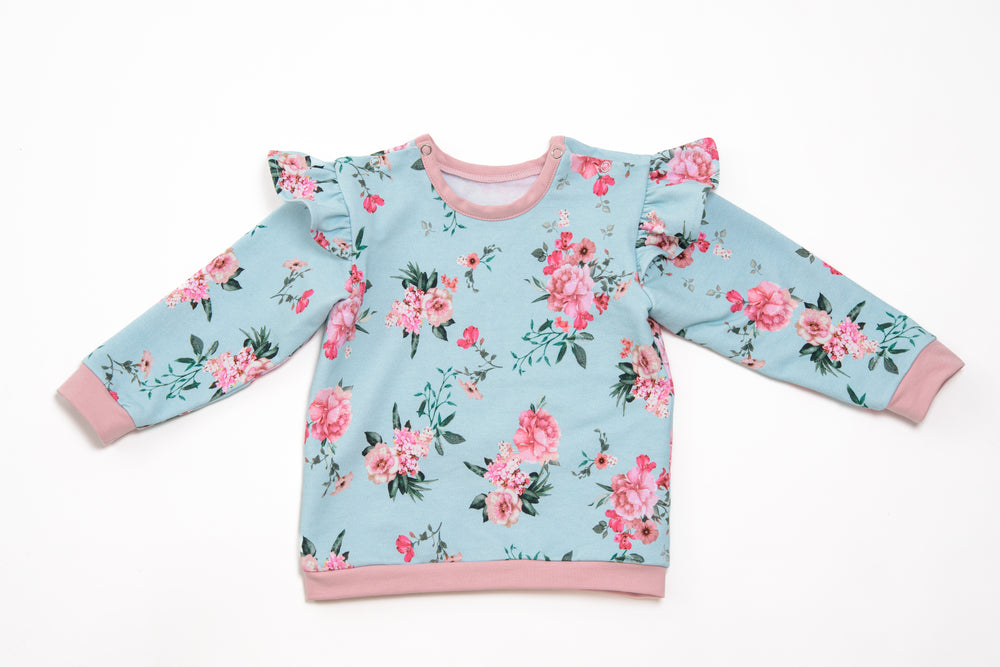 Schnittmuster Baby Sweatshirt mit floralen Mustern, Rüschenärmeln und rosa Details für stilvolle Babykleidung.