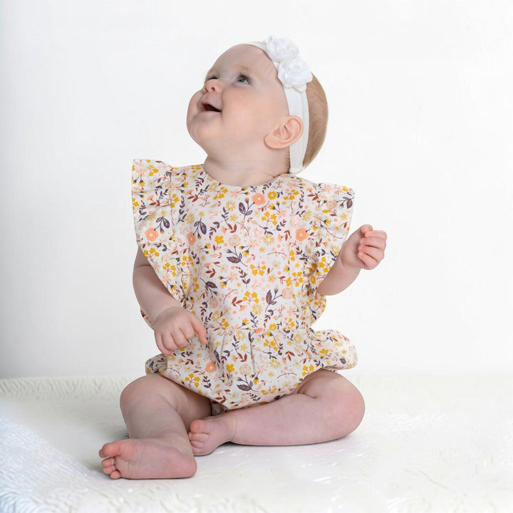 Patternforkids Baby Mädchen Bloomer CHIARA aus floralem Stoff mit Rüschenärmeln, getragen von einem lächelnden Baby.
