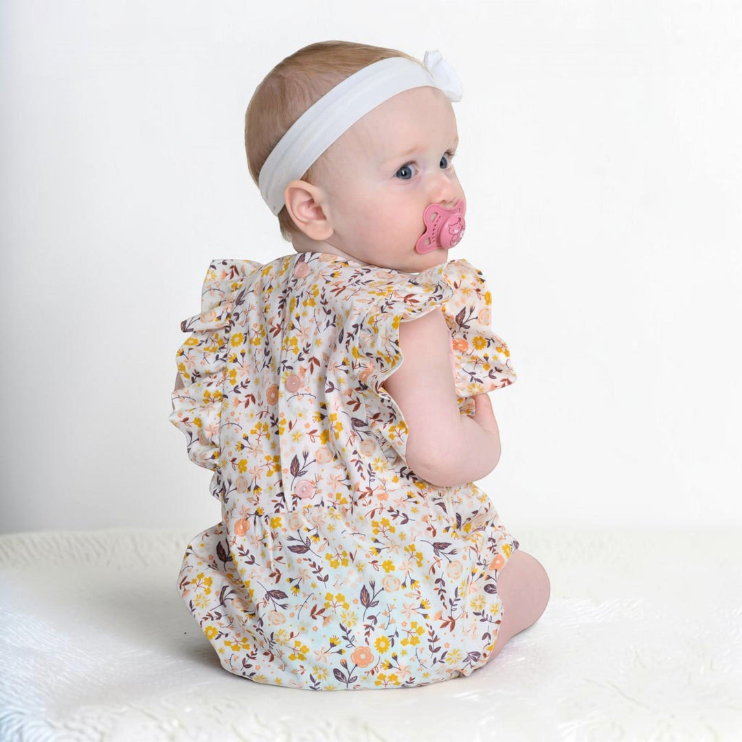 Patternforkids Baby Bloomer CHIARA aus geblümtem Stoff mit Rüschenärmeln an einem Baby mit weißem Stirnband