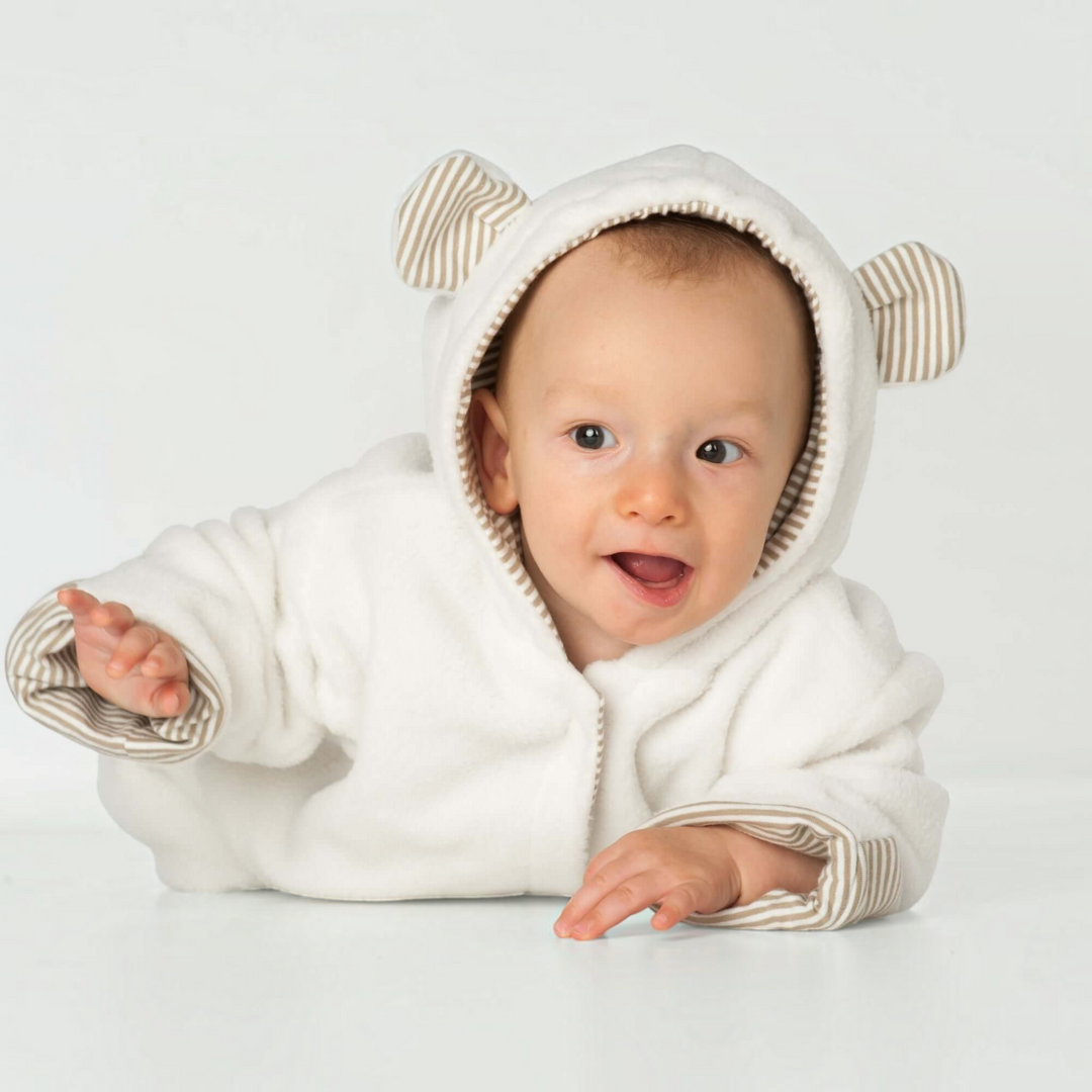Baby trägt einen kuscheligen weißen Kapuzenstrampler CASSIA von Patternforkids mit gestreiften Ohren und Innenfutter