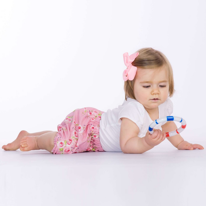 Patternforkids Baby Pumphose STELLA aus rosa Stoff mit Blumenmuster, getragen von einem Baby mit Spielzeug
