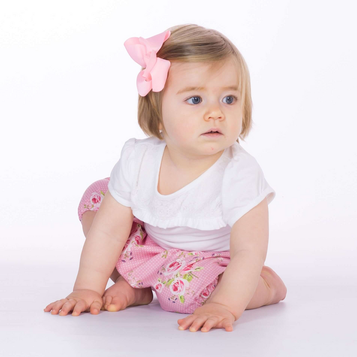 Patternforkids Baby Pumphose STELLA aus rosa Stoff mit Blumenmuster, getragen von einem Kleinkind mit rosa Haarschleife
