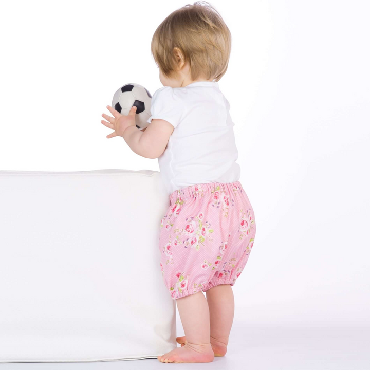 Patternforkids Baby Pumphose STELLA aus rosa Stoff mit Blumenmuster, getragen von einem Kleinkind mit Fußball.