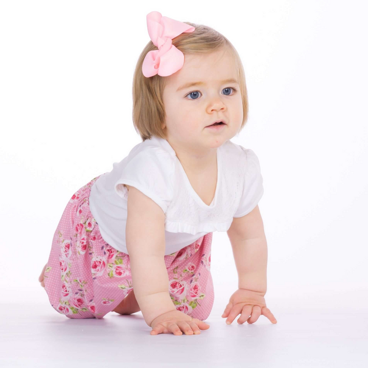 Patternforkids Baby Pumphose STELLA aus rosa Stoff mit Blumenmuster, getragen von einem krabbelnden Kleinkind.