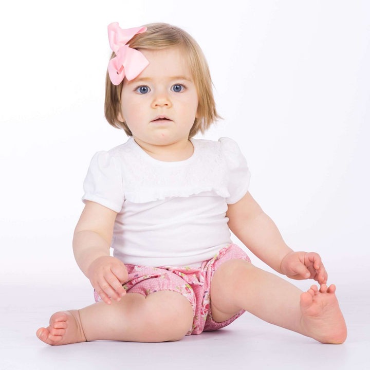 Kleinkind mit rosa Schleife trägt eine Patternforkids Pumphose mit Blumenmuster und elastischen Beinabschlüssen