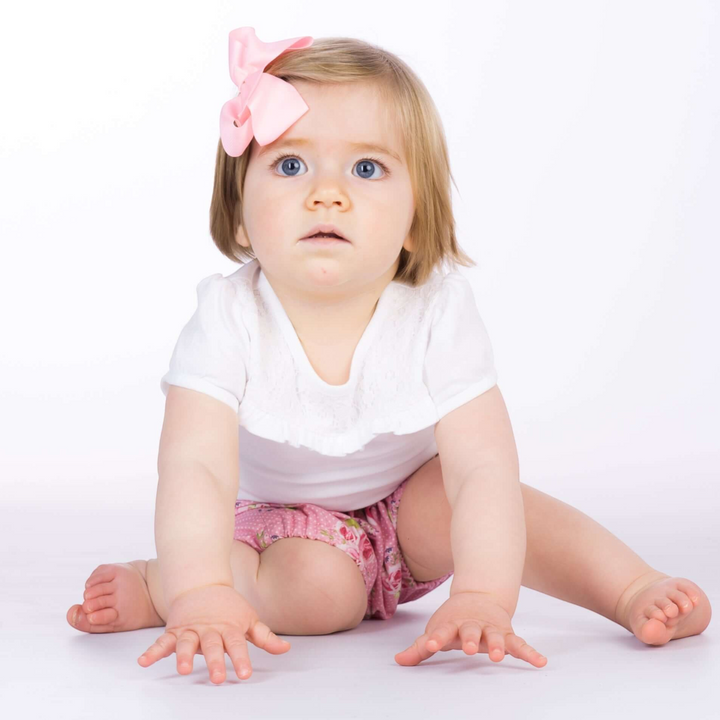 Patternforkids Baby Pumphose Stella als bequeme Bloomers mit Blumenmuster an einem sitzenden Kleinkind mit Haarschleife