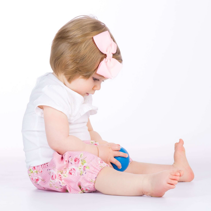 Patternforkids Baby Pumphose STELLA mit Blumenmuster, getragen von einem Kleinkind mit rosa Haarschleife
