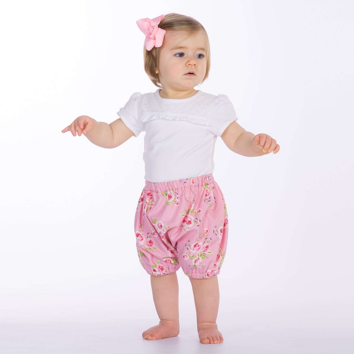 Patternforkids Baby Pumphose STELLA mit Blumenmuster in Rosa, getragen von einem Kleinkind mit rosa Haarschleife.