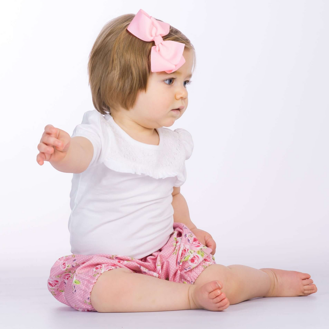 Patternforkids Baby Pumphose Stella mit Blumenmuster in Rosa, getragen von einem Kleinkind mit weißem Shirt und Schleife