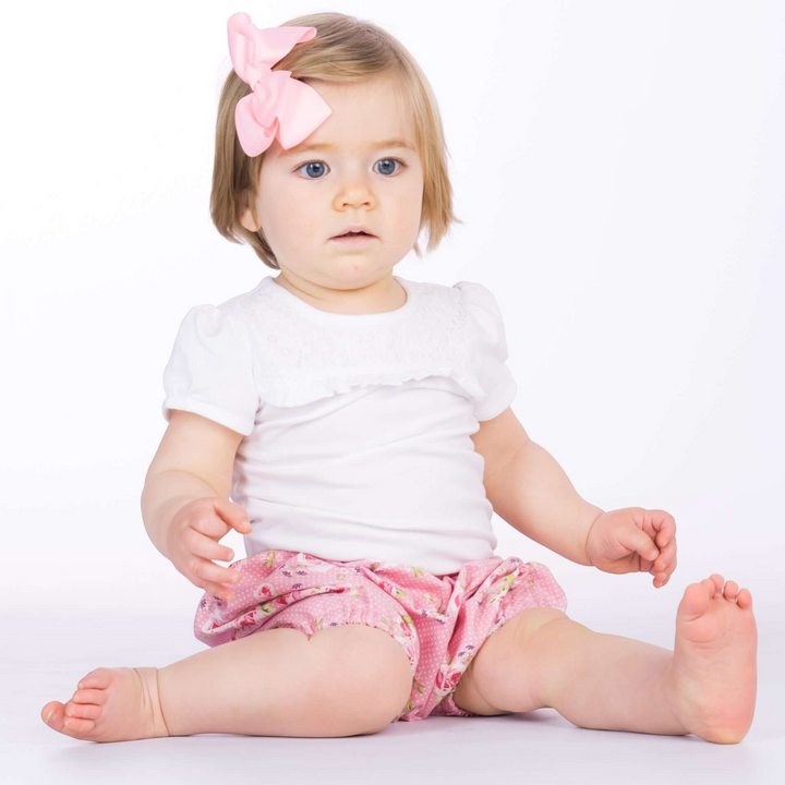Kleinkind trägt Patternforkids Pumphose STELLA mit Blumenmuster in Rosa, kombiniert mit weißem T-Shirt und Haarschleife