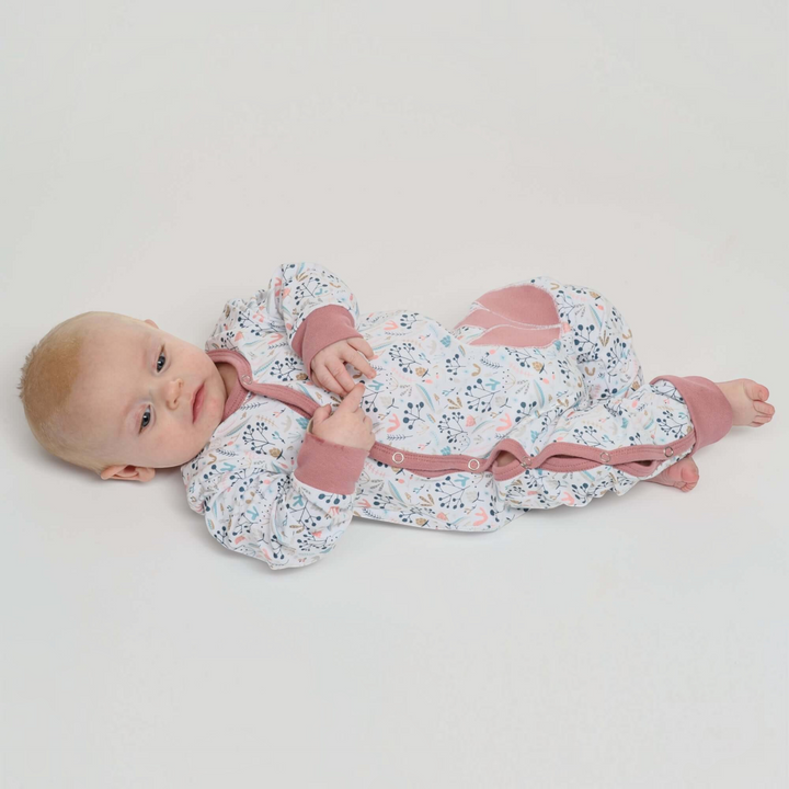 Patternforkids Baby Strampler LISA mit Blumenmuster, Druckknöpfen und rosa Bündchen, getragen von einem Baby.