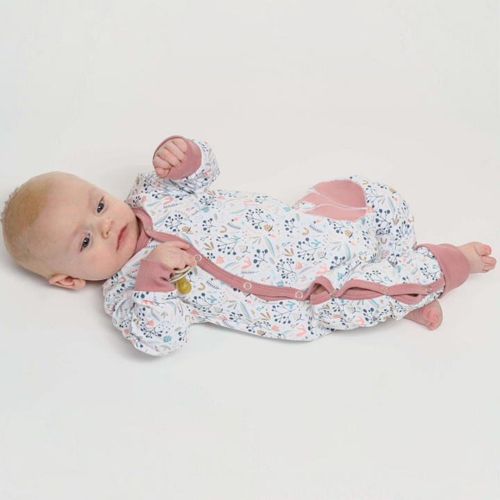 Patternforkids Baby Strampler LISA mit Blumenmuster und Druckknöpfen, getragen von einem Baby auf weißem Hintergrund
