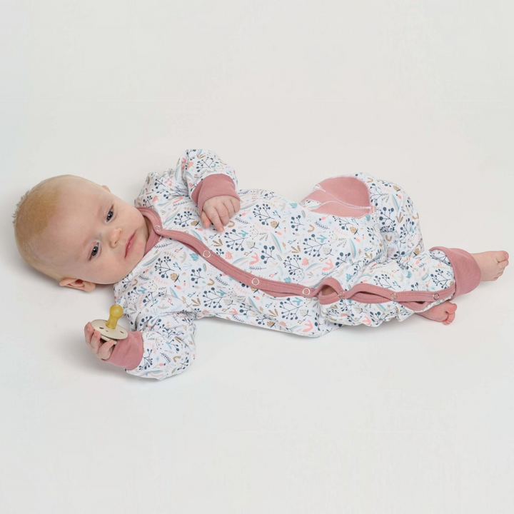 Patternforkids Baby Strampler LISA mit Blumenmuster, Druckknöpfen und rosa Bündchen, getragen von einem Baby.