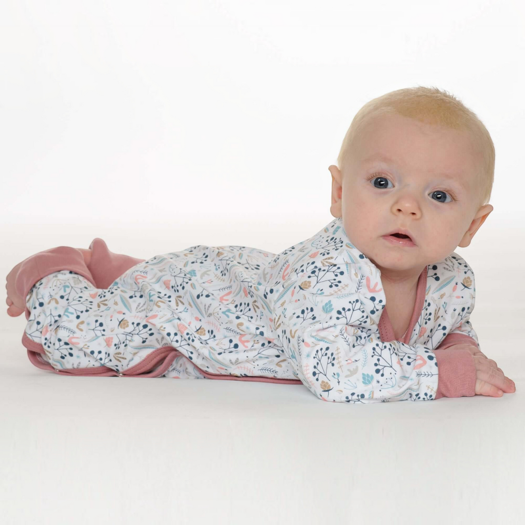 Patternforkids Baby Strampler LISA mit Blumenmuster, Langarm und rosa Bündchen, liegendes Baby auf weißem Hintergrund