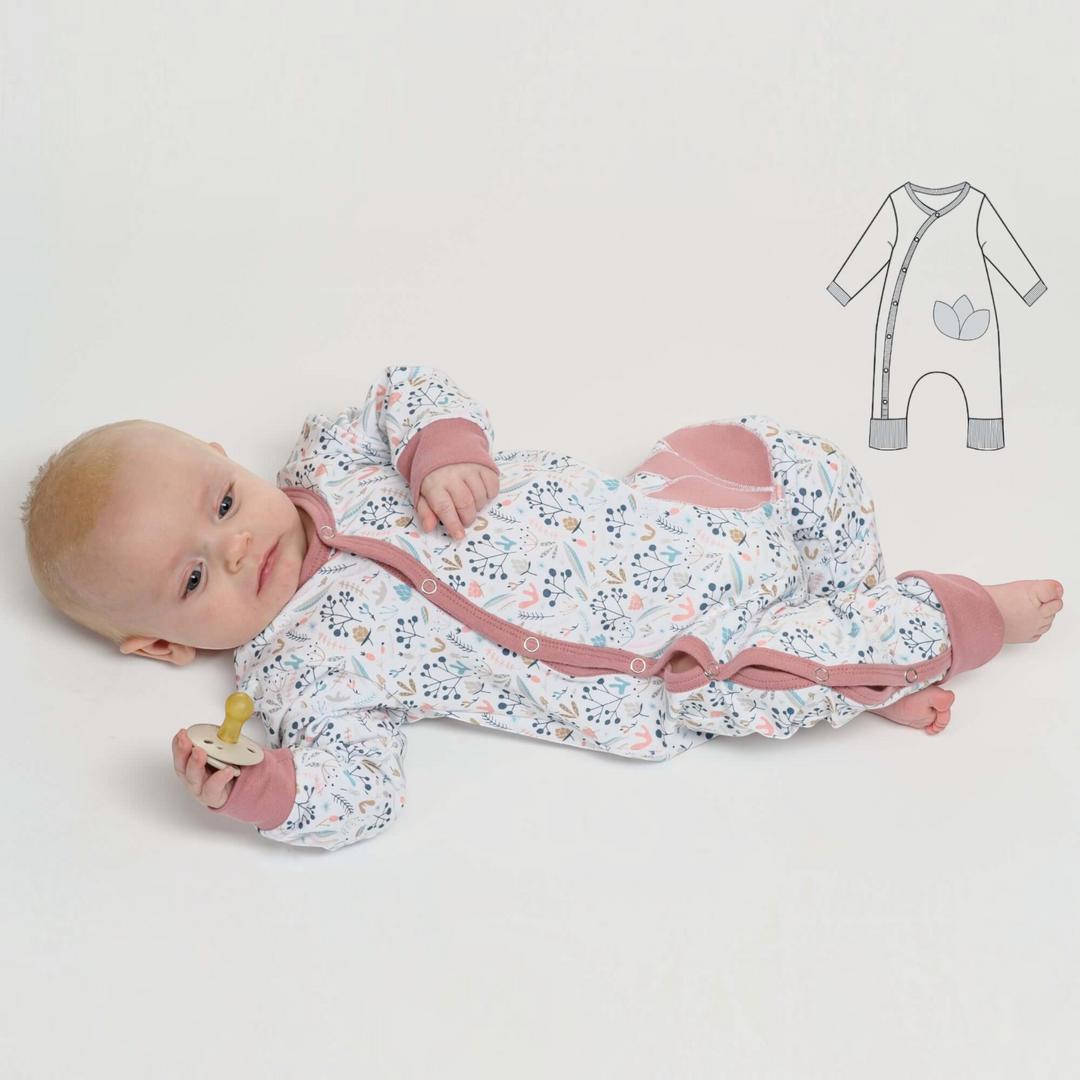 Patternforkids Baby Strampler LISA mit Blumenmuster, Druckknöpfen und rosa Bündchen, getragen von einem Baby.