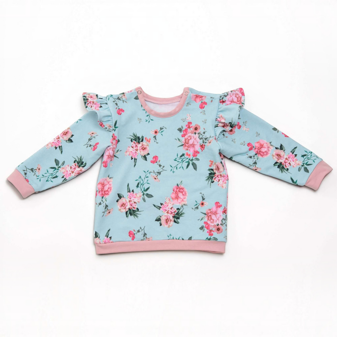 Patternforkids Baby Sweatshirt SOPHIE mit Blumenmuster, Rüschen an den Schultern und rosa Bündchen auf weißem Grund.