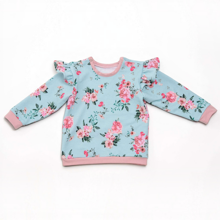 Patternforkids Baby Sweatshirt SOPHIE mit Blumenmuster, Rüschen an den Schultern und rosa Bündchen auf weißem Grund.