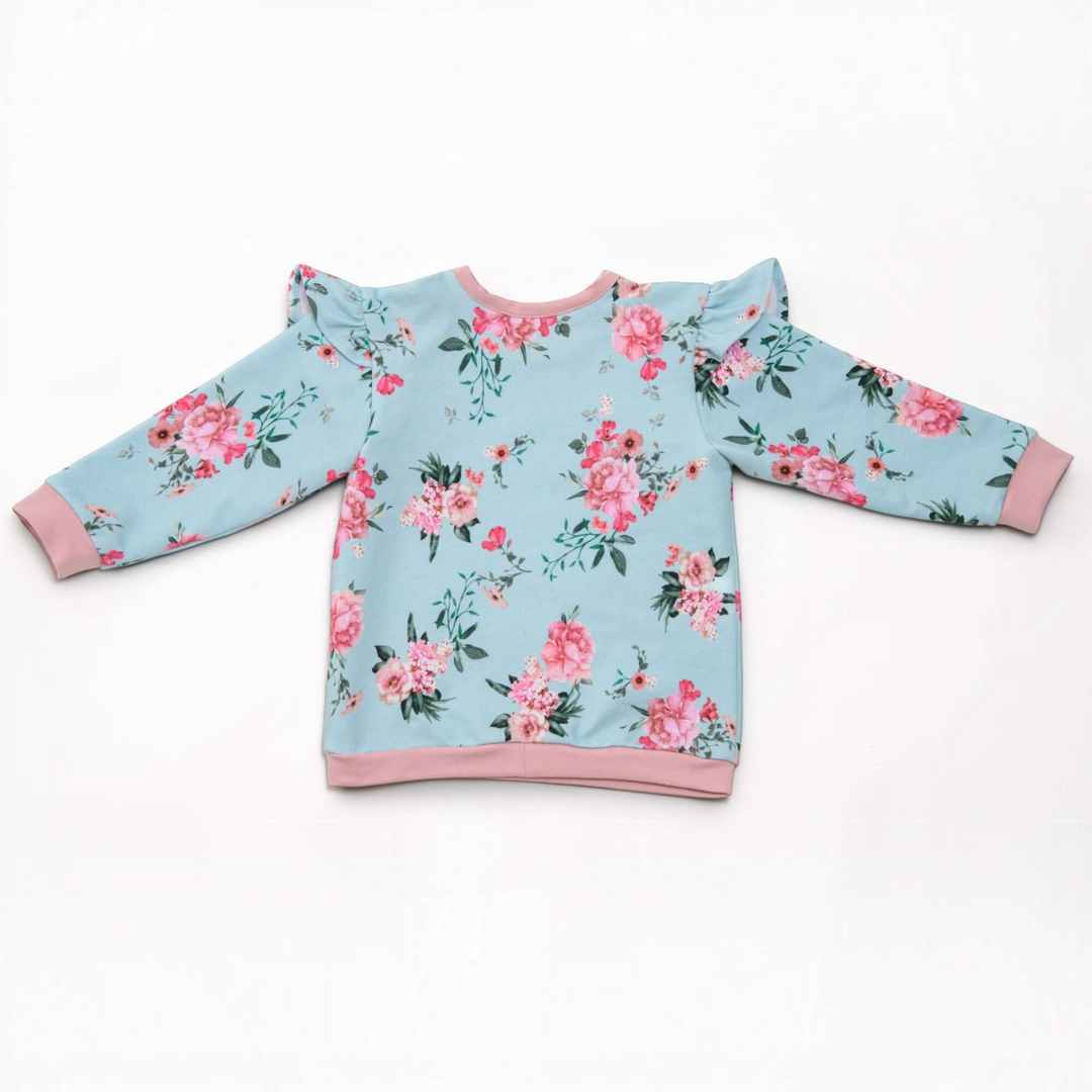 Patternforkids Baby Sweatshirt SOPHIE mit Blumenmuster, Rüschen an den Schultern und rosa Bündchen auf weißem Grund.