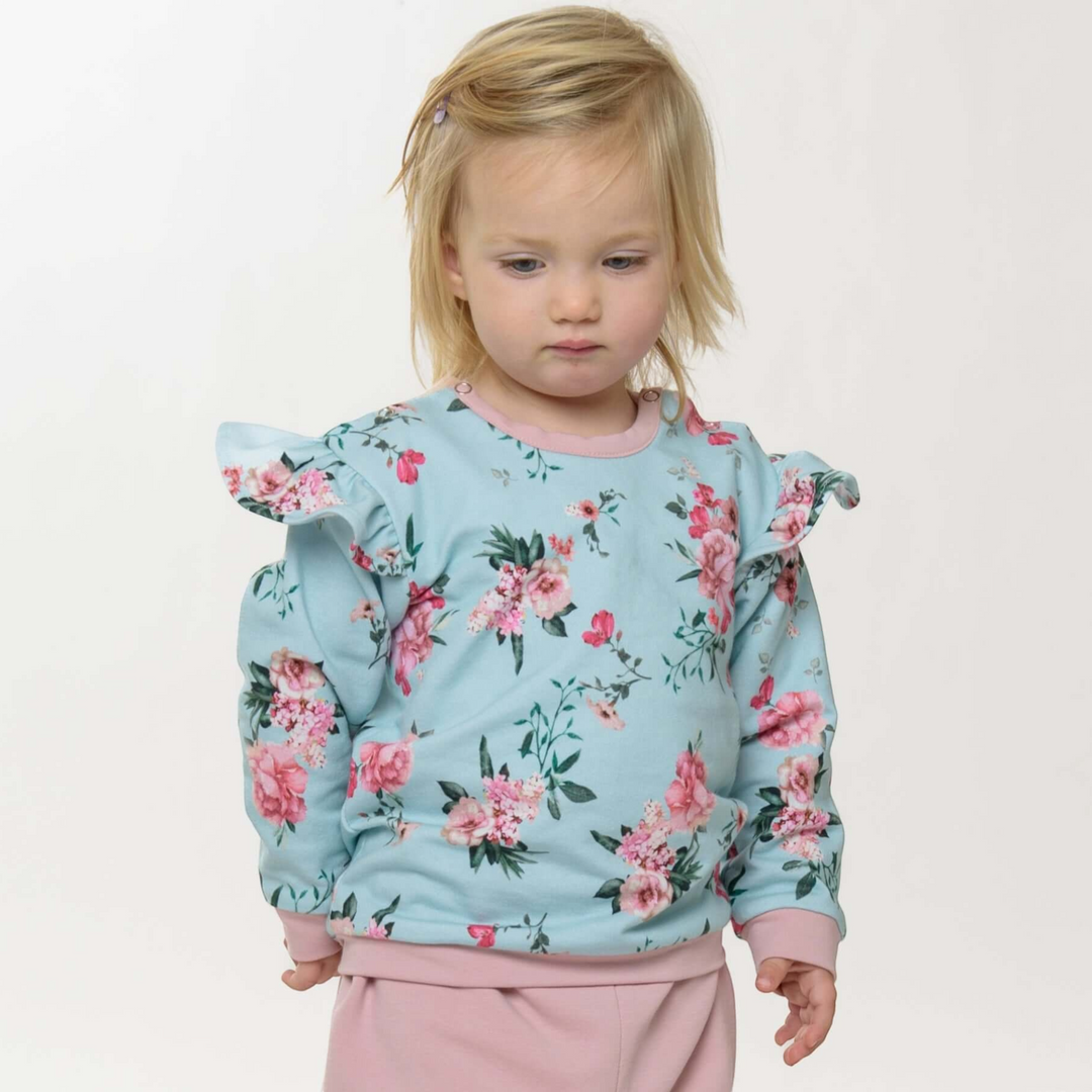 Patternforkids Baby Sweatshirt Sophie mit Rüschen und floralem Muster in Hellblau und Rosa an einem Kleinkind