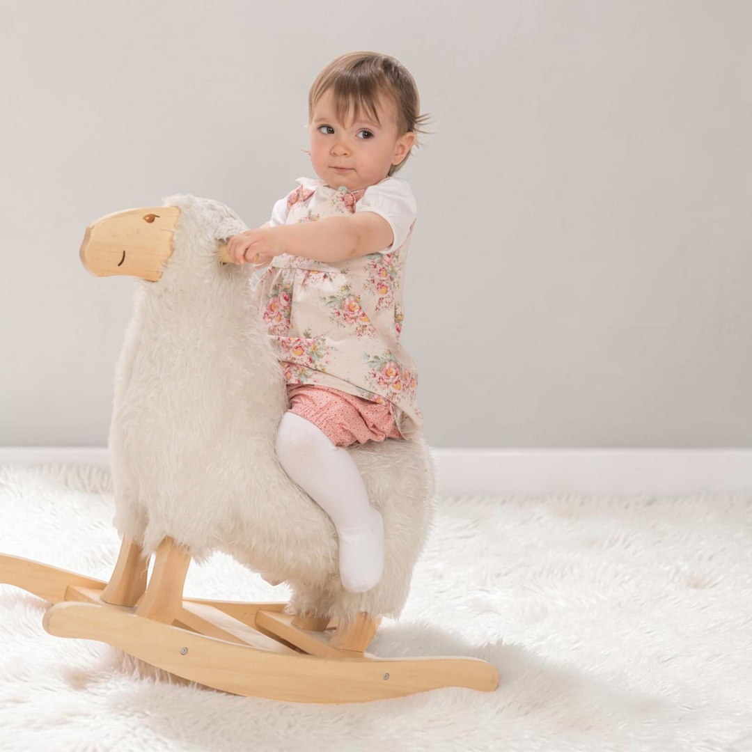 Kleinkind auf einem Schaukel-Schaf trägt das Patternforkids Baby-Twinset mit Blumenkleid und rosa Pumphose