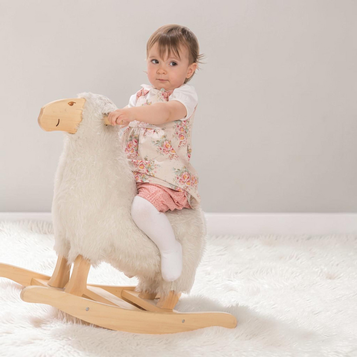 Kleinkind auf einem Schaukel-Schaf trägt das Patternforkids Baby-Twinset mit Blumenkleid und rosa Pumphose