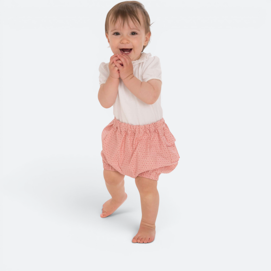 Patternforkids Baby-Twinset mit weißem Oberteil und rosa gemusterter Pumphose mit Rüschen an einem lachenden Baby