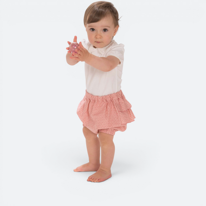 Kleinkind trägt ein Patternforkids Twinset mit weißem Oberteil und rosa Pumphose mit Rüschen auf weißem Hintergrund