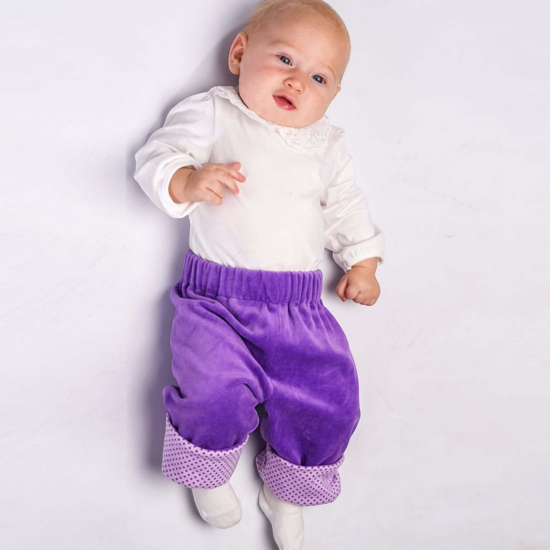 Patternforkids Baby Wendehose FIORETTO aus lila Samtstoff mit gepunkteten Beinbündchen an einem liegenden Baby