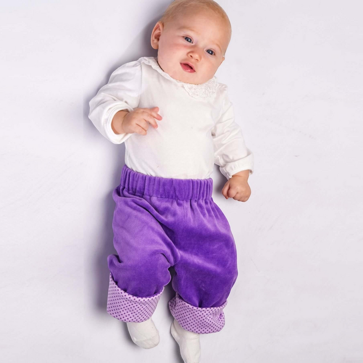 Patternforkids Baby Wendehose FIORETTO aus lila Samtstoff mit gepunkteten Beinbündchen an einem liegenden Baby