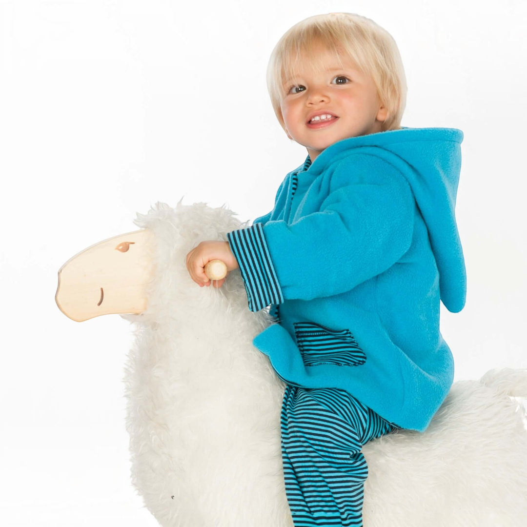 Patternforkids Babyjacke Toretto aus blauem Fleece mit Zipfelkapuze, getragen von einem Kind auf einem Schaukelpferd