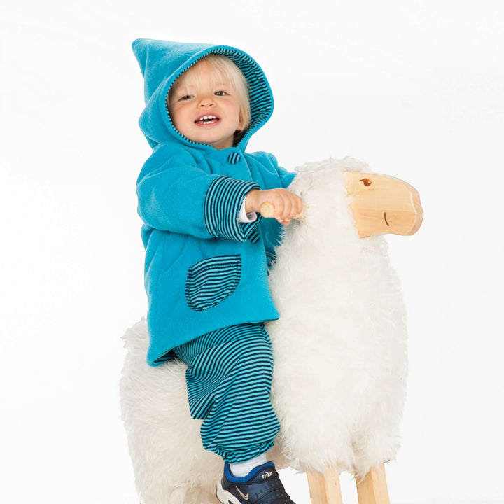 Patternforkids Babyjacke Toretto Schnittmuster mit blauer Zipfelkapuze und gestreiften Details an einem Kind auf Schaukelpferd