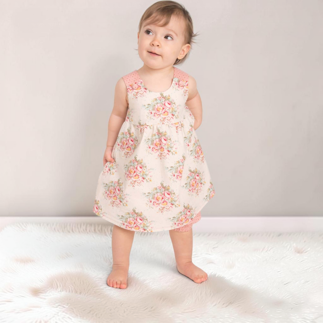 Patternforkids Babykleid Clara mit Blumenmuster und passender Pumphose an einem Kleinkind auf einem Fellteppich
