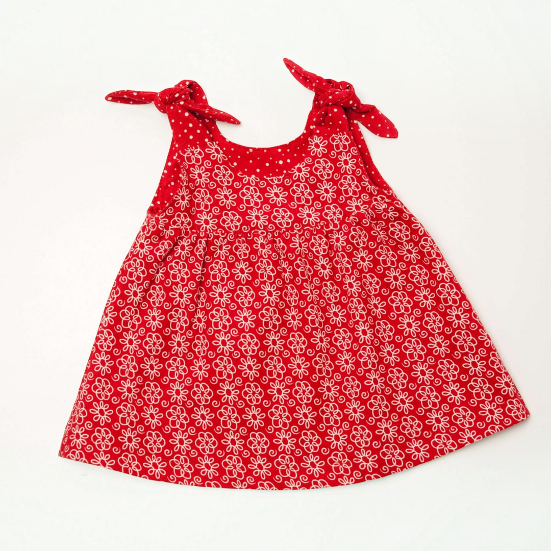 Patternforkids Babykleid Clara mit rotem Blumenmuster und gebundenen Trägern aus Baumwolle auf weißem Hintergrund