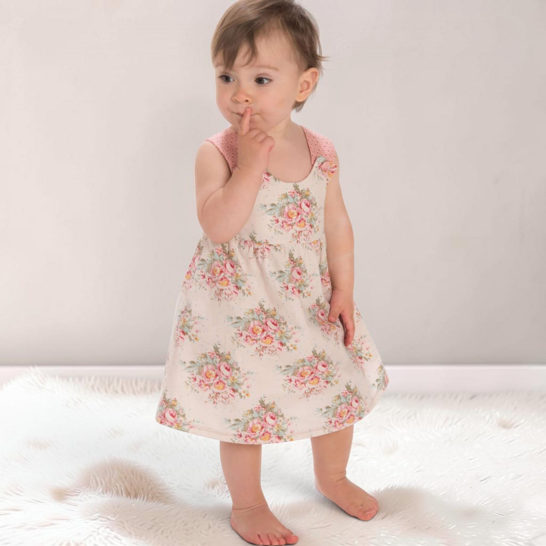 Kleinkind trägt ein florales Patternforkids Sommerkleid mit rosa gepunkteten Trägern auf einem flauschigen Teppich