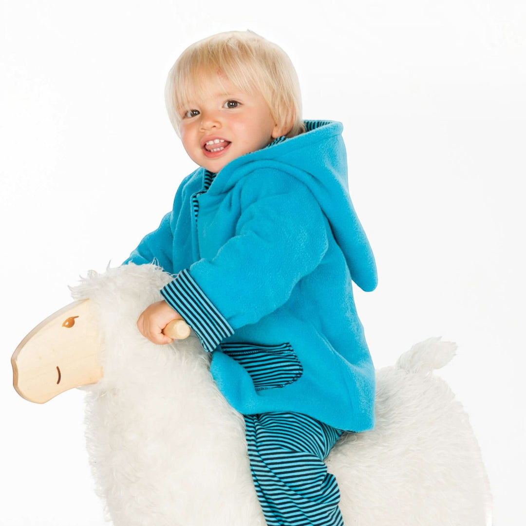 Kind auf Schaukelpferd trägt eine blaue Patternforkids Fleecejacke mit Zipfelkapuze und gestreiften Details