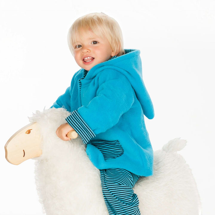 Kind auf Schaukelpferd trägt eine blaue Patternforkids Fleecejacke mit Zipfelkapuze und gestreiften Details