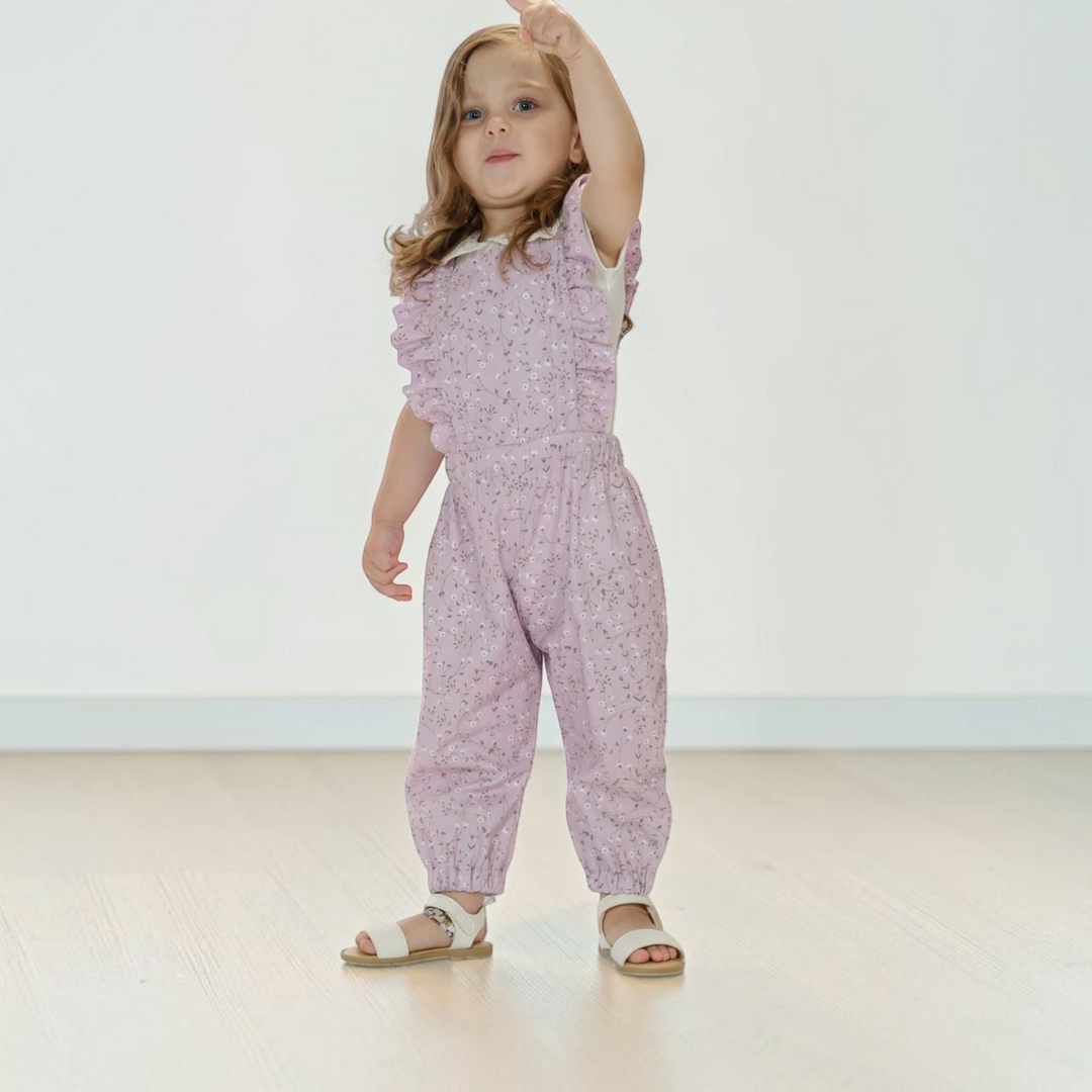 Patternforkids Latzhose Daisy aus fliederfarbenem Stoff mit Blumenmuster, Rüschen an den Trägern und elastischem Bund