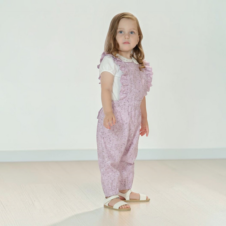 Patternforkids Latzhose DAISY in zartem Flieder mit Rüschen und Blumenmuster an einem kleinen Mädchen