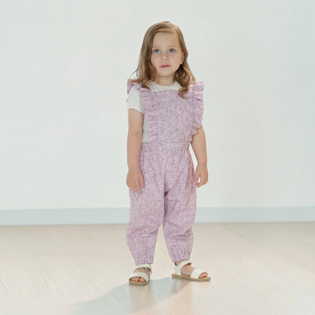 Patternforkids Latzhose Daisy aus fliederfarbenem Stoff mit Rüschen an einem kleinen Mädchen