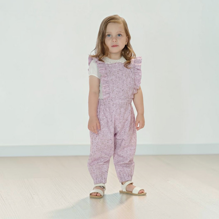 Patternforkids Latzhose Daisy aus fliederfarbenem Stoff mit Rüschen an einem kleinen Mädchen