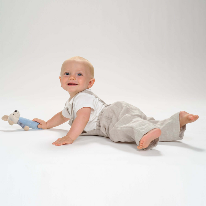 Patternforkids Kleinkind Latzhose MAX aus beigem Leinenstoff, getragen von einem Baby mit Kuscheltier